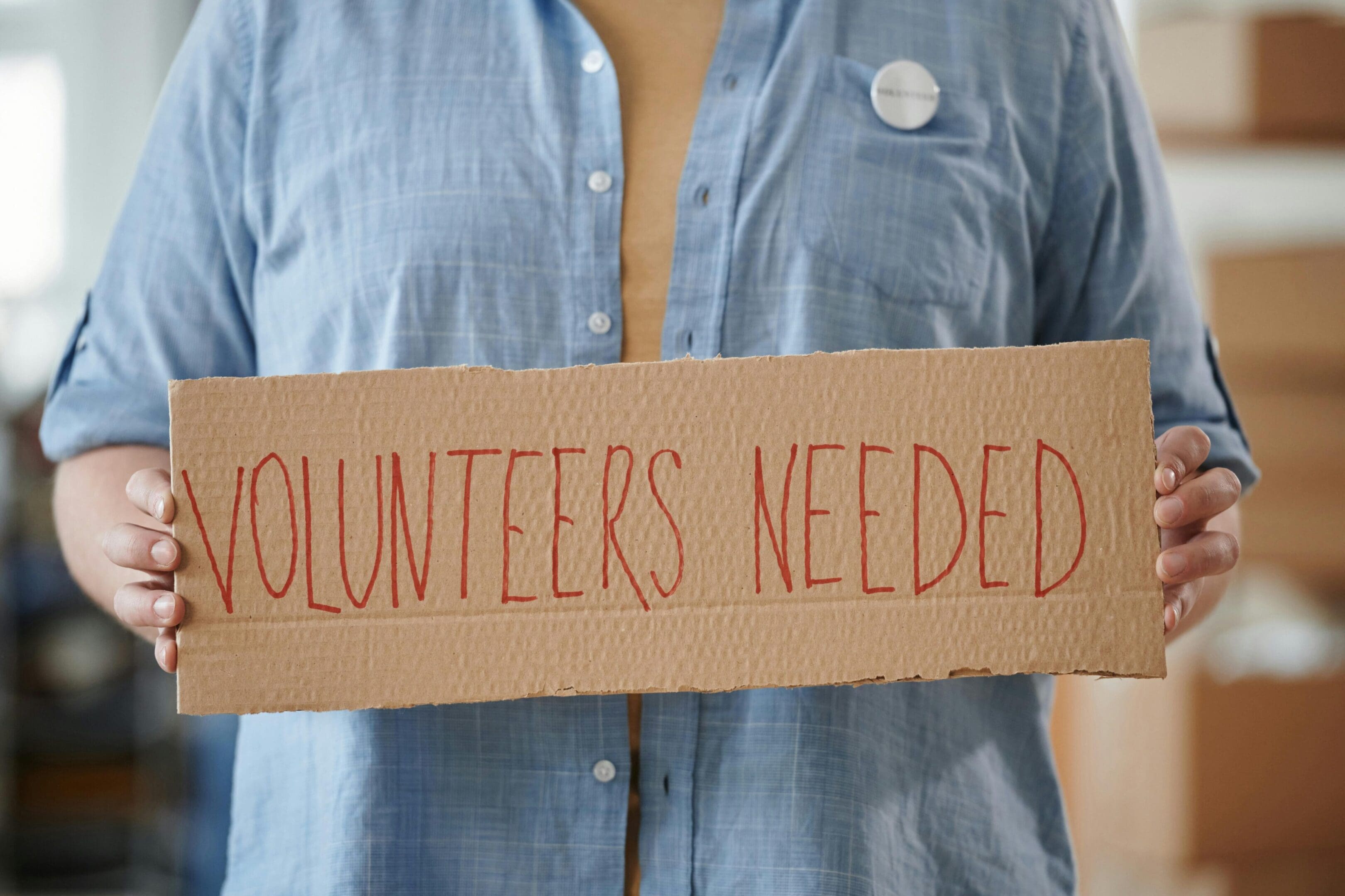 A person holding up a sign that says volunteers needed.